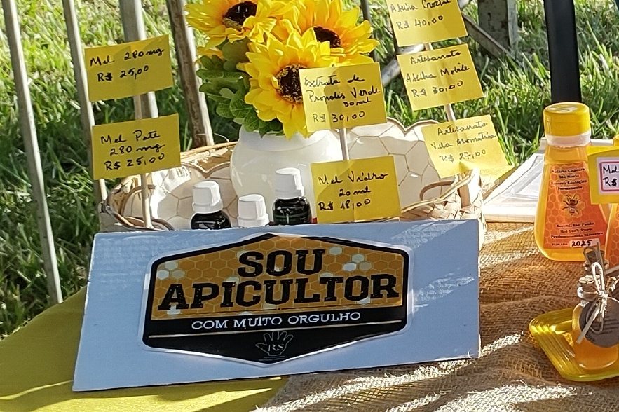 Canto da mesa com a placa ‘Sou apicultor com muito orgulho’, girassóis e potes de mel.