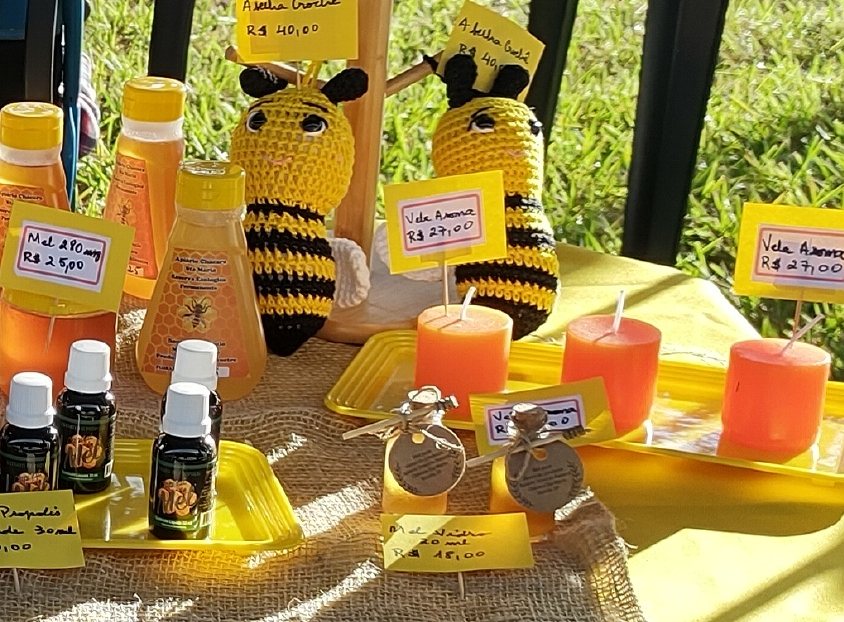 Extratos de própolis, velas aromáticas e abelhas de crochê expostas na mesa da feira.